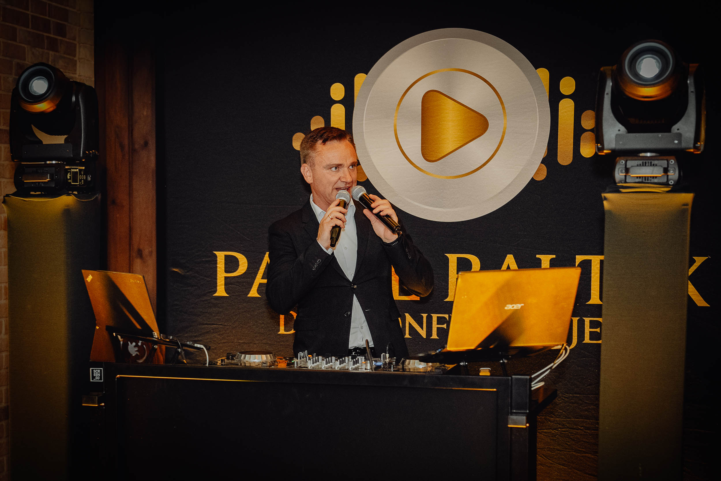 DJ Paweł Bałtyk na weselu w Zajeździe Sokołda wita parę młodą mówiąc jednocześnie do dwóch mikrofonów.