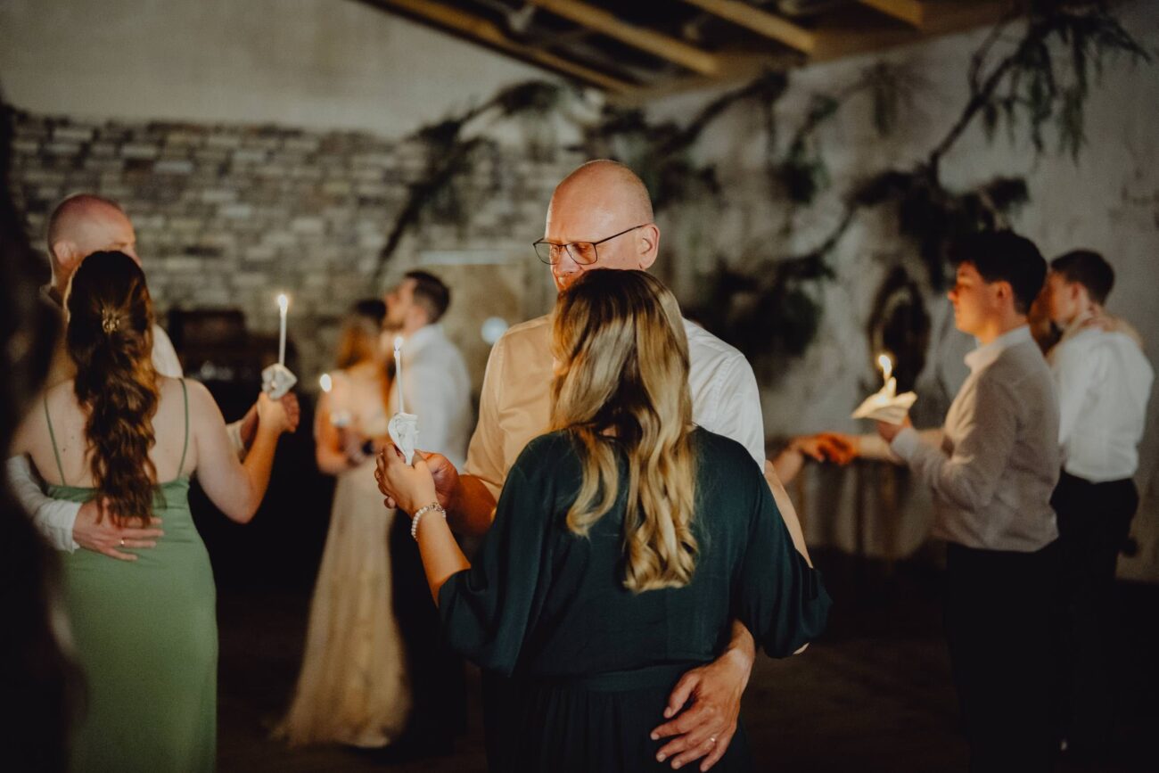 Atrakcja weselna ze świecami na parkiecie. Goście tańczą w parach trzymając w rękach cienkie świece. Jest ciemno.