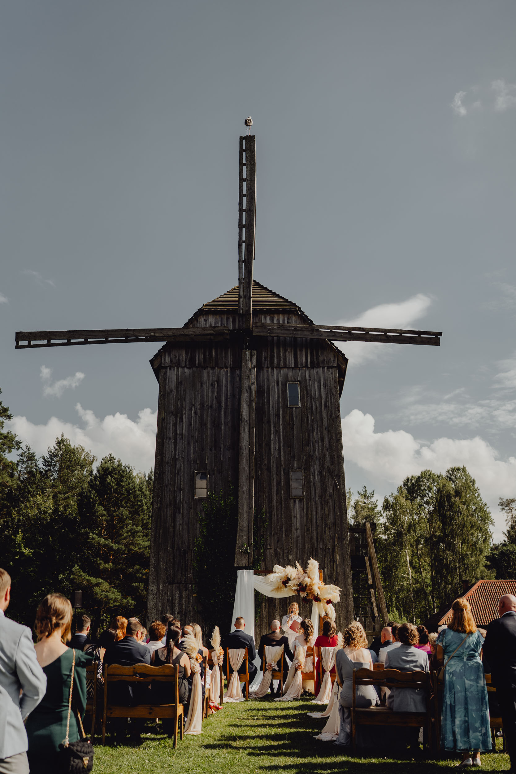 Ceremonia ślubne w plenerze pod starym wiatrakiem. Bocian siada na ramieniu wiatraka w czasie ślubu.