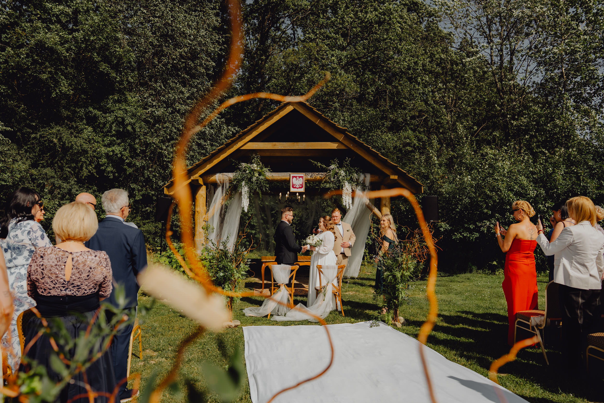 Ceremonia ślubna w naturalnym plenerze wśród drzew. Para młoda stoi i składa przysięgę.