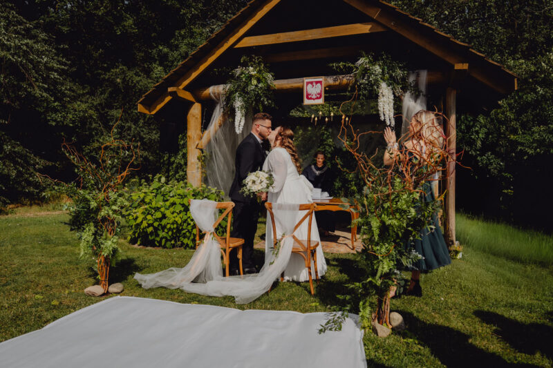 Para młoda całuje się zaraz po przysiędze małżeńskiej podczas swojego ślubu cywilnego w plenerze wśród zieleni.