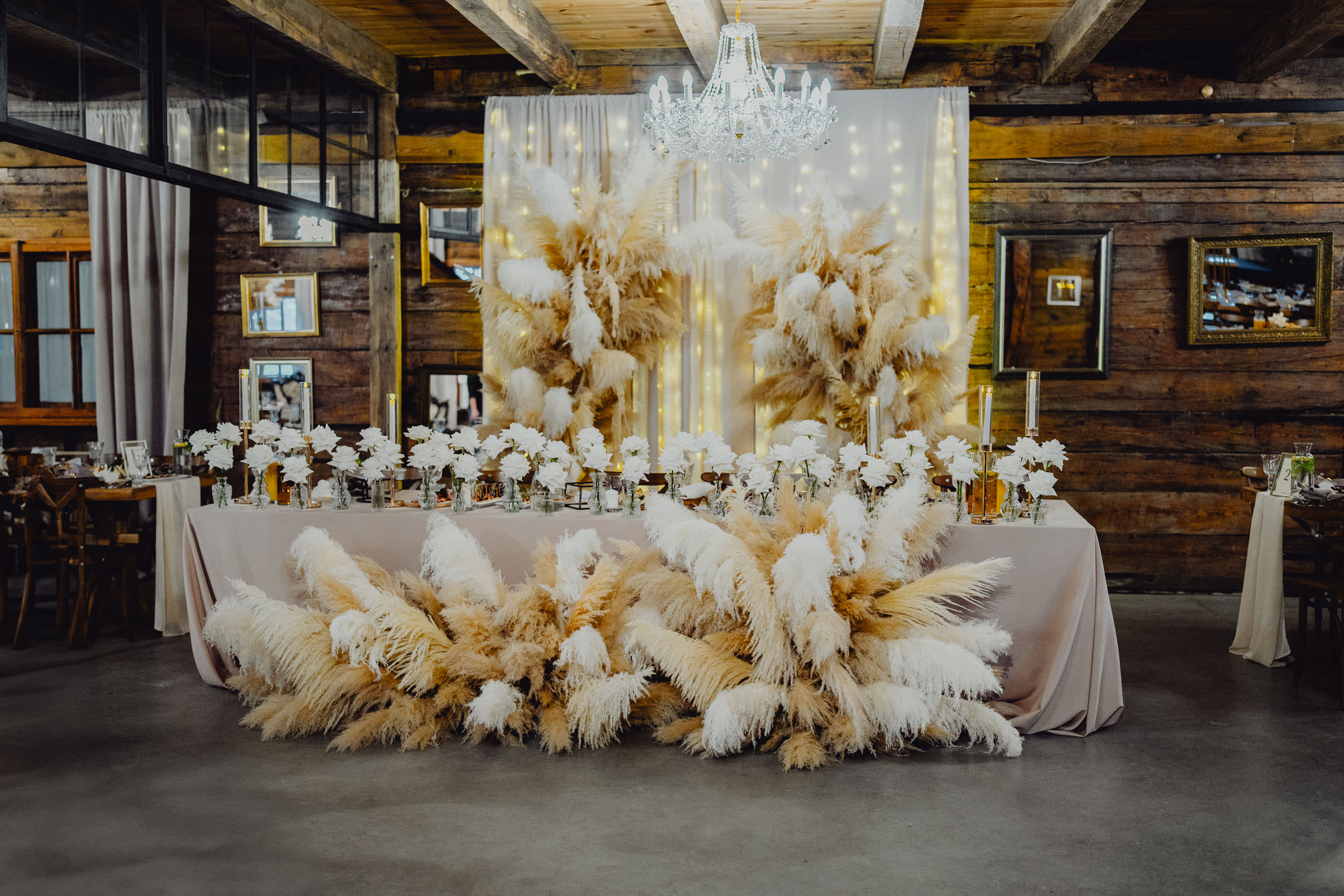 Przepiękna dekoracja stoły Pary Młodej w Dworze Modrzewiowym Majątku Howieny. Widać dziesiątki białych róż, świec oraz piękne wysokie trawy.