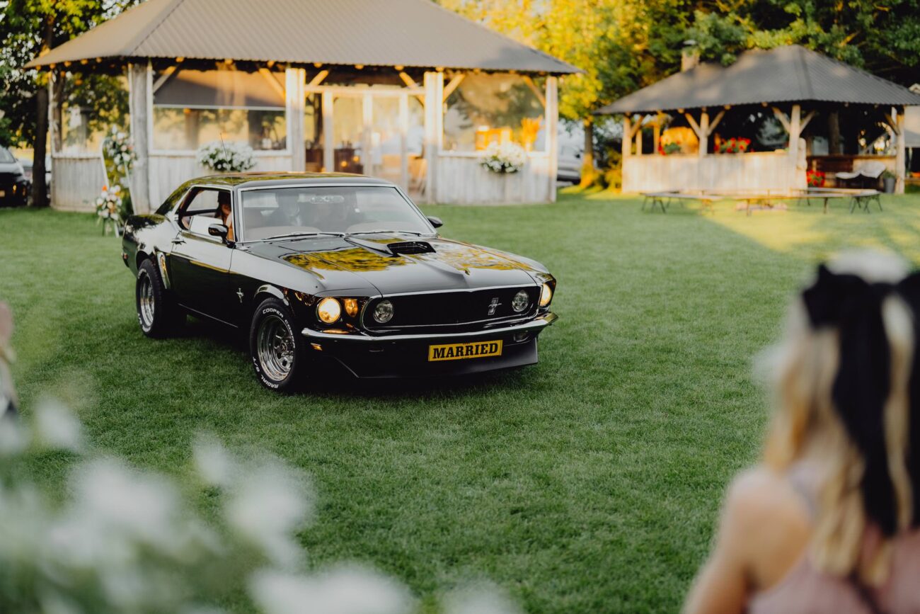 Auto do ślubu Ford Mustang, Chevy Impala stoi przed salą weselną na trawie. Para Młoda jest jeszcze w środku