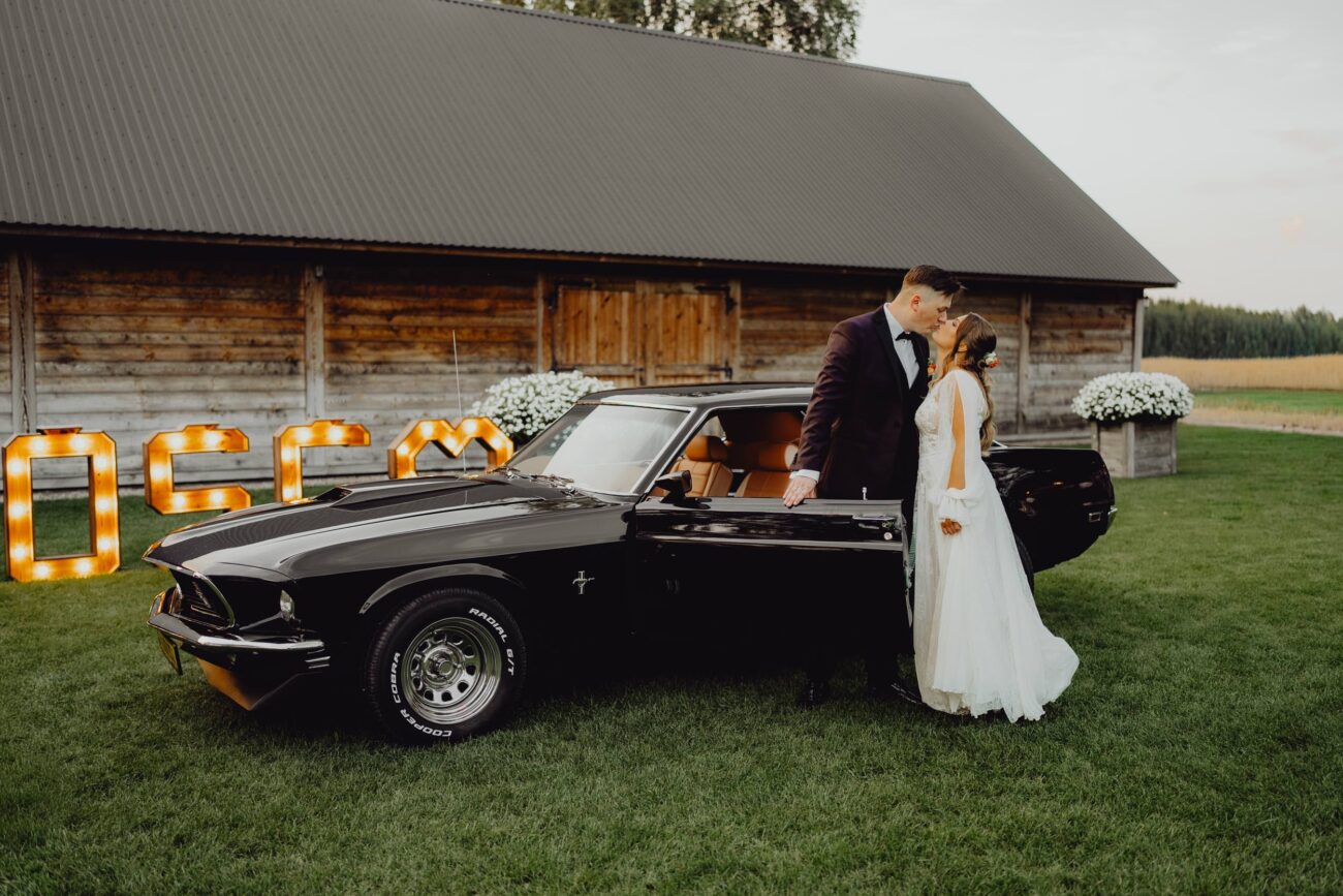 Para Młoda całuj się przy samochodzie do ślubu Ford Mustang, Chevy Impala.