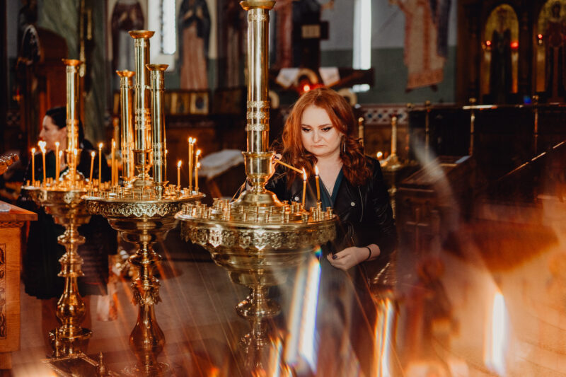 Kobieta zapala świecę w intencji pary młodej podczas ślubu cerkiewnego