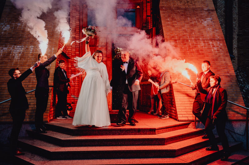 Młoda Para wychodzi ze swojego ślubu w cerkwii, przywitana przez gości czerwonymi racami