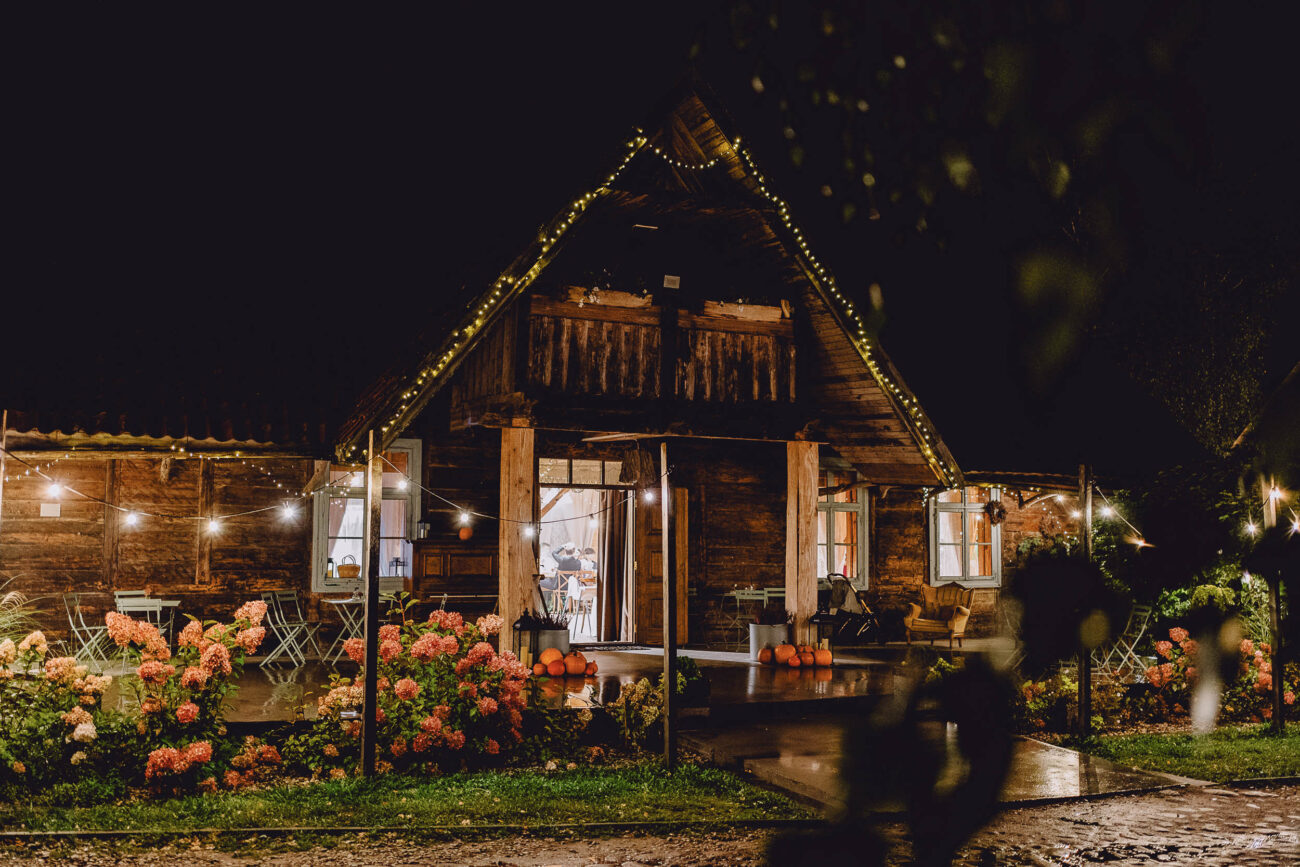 Wejście do Dworku Rustykalnego w Majątku Howieny. Widać piękną podlaską drewnianą architekturę oraz kwiaty przed stodołą.