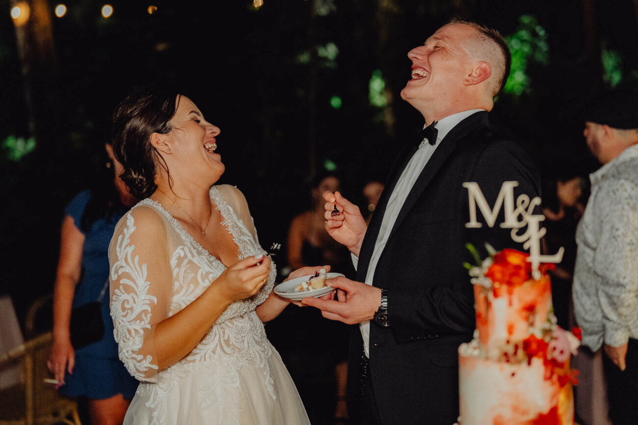 Szczęśliwa Para młoda smieje się podczas krojenia tortu weselnego w Stodole weselnej Kiszukówka.