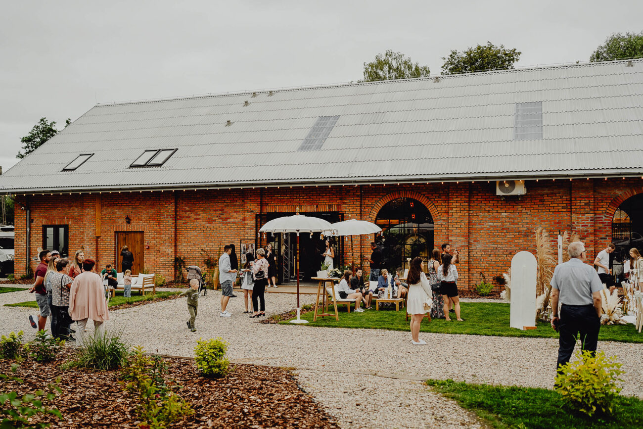 Stodoła Weselna Między Travami, widać gości weselnych przed stodołą pod parasolami.