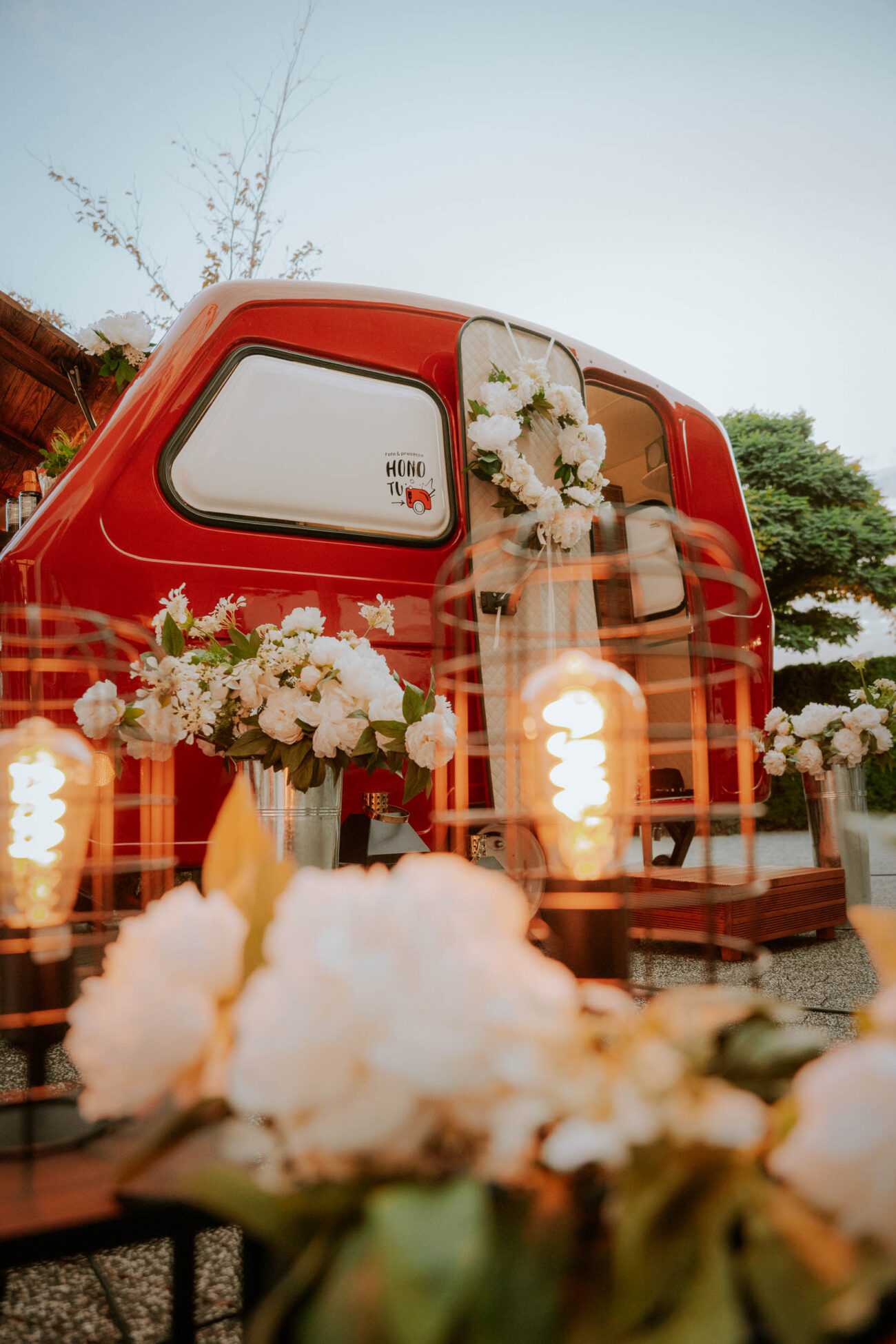Fotoprzyczepa HONOTU wśród białych kwiatów i innych weselnych dekoracji.
