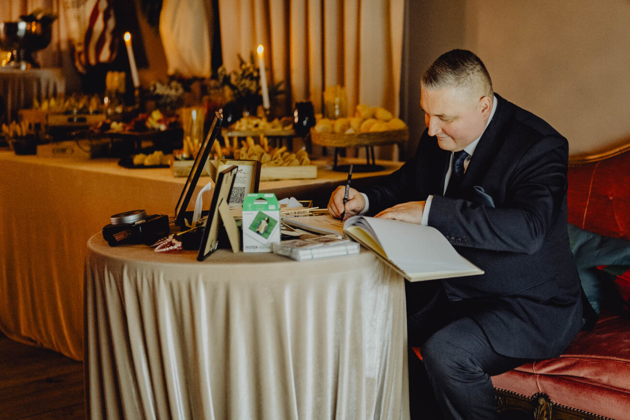 Ojciec panny młodej spisuje życzenia weselne w księdze gości